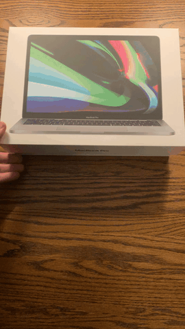 A gif of someone opening a MacBook pro box and setting the computer on a wooden table.